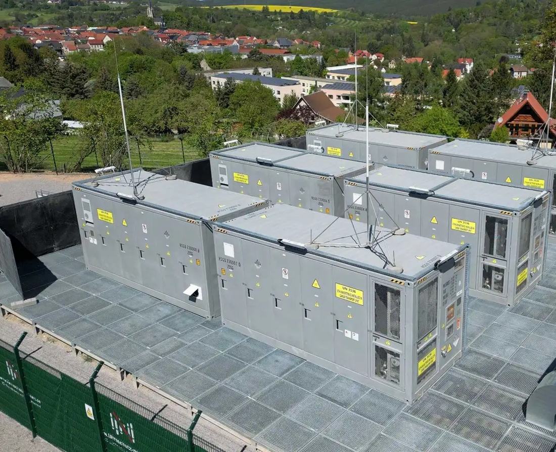 Batteriespeicher in Containerbauweise auf einem eingezäunten Betriebsgelände, aufgestellt auf Fundamenten mit Kiesbett und Wechselrichterstationen